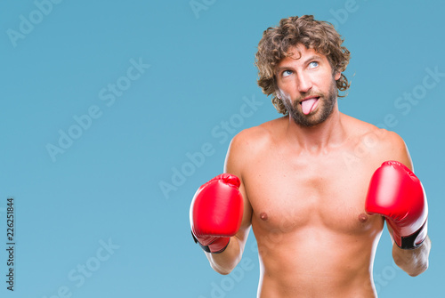 Handsome hispanic boxer man wearing boxing gloves over isolated background sticking tongue out happy with funny expression. Emotion concept.