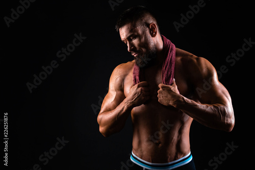 Muscular man is showing his torso with towel on the shoulders