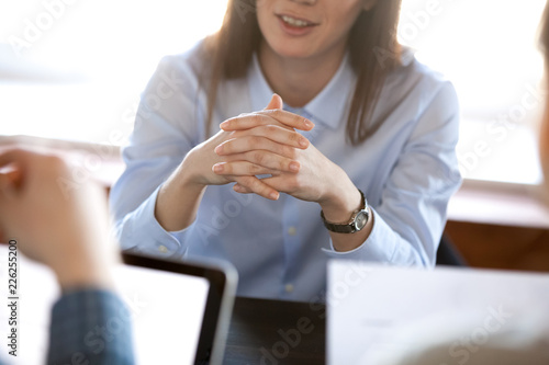 Smiling woman attentively listening to partners concentrated on business negotiations, nonverbal communication concept, focus on locked crossed fingers, clenched hands gesture close up view