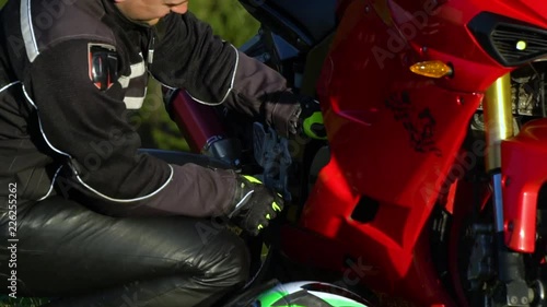A guy on a motorcycle. Young handsome guy with his motorcycle in the mountains. The guy is sitting near his motorcycle. He is checking his motorcycle. Close-up.