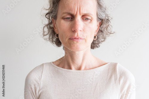 Close up head and shoulders view of middle aged woman with grey hair and cream top frowning and showing wrinkles (selective focus) photo