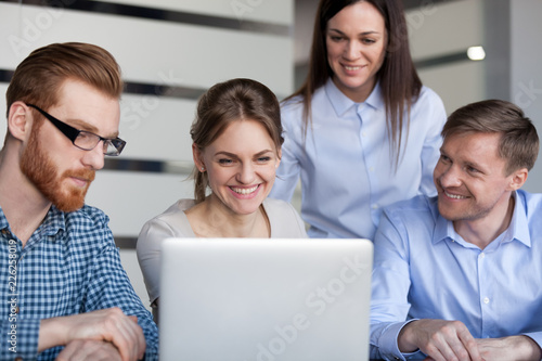 Happy smiling office employees colleagues project team having fun looking at laptop using business software excited by online result growth, satisfied with successful teamwork, good news or success