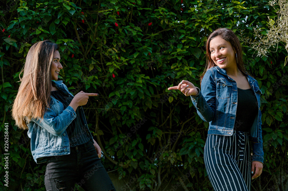 Fototapeta premium Cheerful friends are gossiping in the park. The girls are pointing with their finger and laughing.