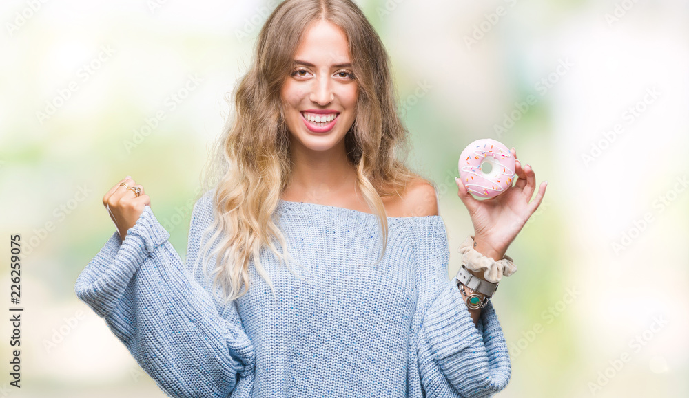 Beautiful young blonde woman eating pink donut over isolated background screaming proud and celebrating victory and success very excited, cheering emotion Beautiful young blonde woman eating pink donut over isolated background screaming proud and celebrating victory and success very excited, cheering emotion