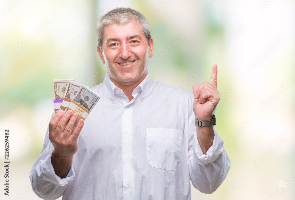Handsome senior man holding bunch of money over isolated background surprised with an idea or question pointing finger with happy face, number one Handsome senior man holding bunch of money over isolated background surprised with an idea or question pointing finger with happy face, number one