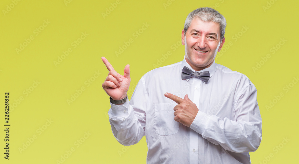 Fototapeta premium Handsome senior man wearing bow tie over isolated background smiling and looking at the camera pointing with two hands and fingers to the side.