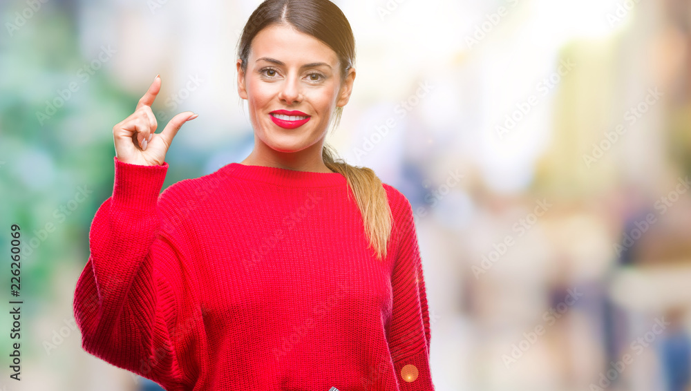 Young beautiful business woman wearing winter sweater over isolated background smiling and confident gesturing with hand doing size sign with fingers while looking and the camera. Measure concept.