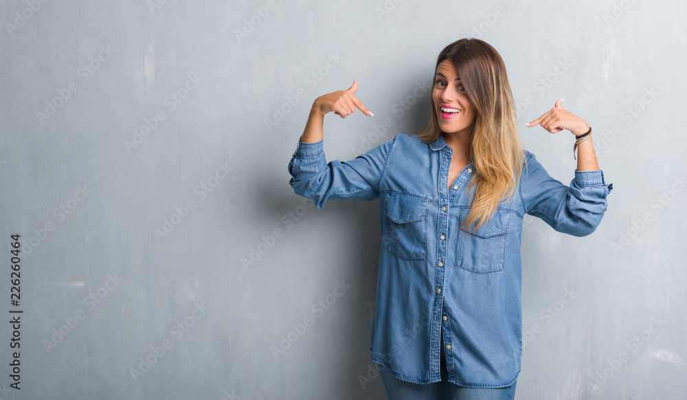 Φωτογραφία Young adult woman over grunge grey wall wearing denim outfit looking confident with smile on face, pointing oneself with fingers proud and happy