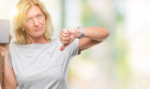 Middle age blonde woman showing blank screen of smartphone over isolated background with angry face, negative sign showing dislike with thumbs down, rejection concept