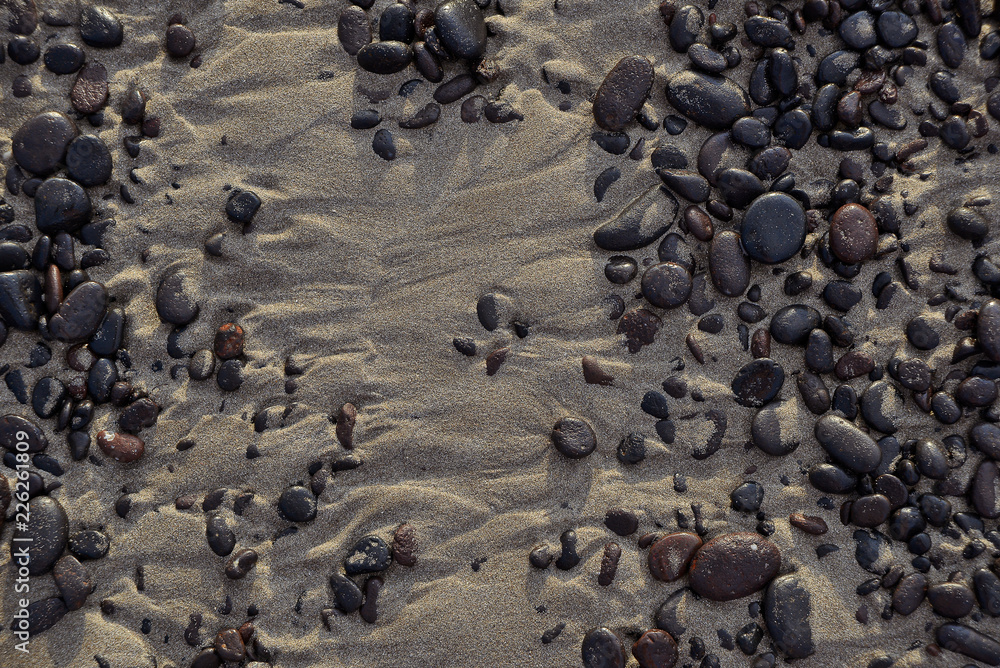 smooth, wave-rolled volcanic stones on wet sand in a low tide smooth, wave-rolled volcanic stones on wet sand in a low tide
