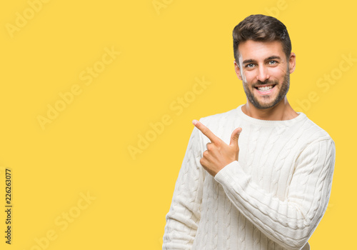 Young handsome man wearing winter sweater over isolated background cheerful with a smile of face pointing with hand and finger up to the side with happy and natural expression on face