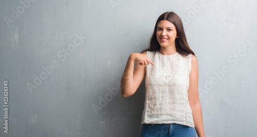 Young brunette woman over grunge grey wall with surprise face pointing finger to himself