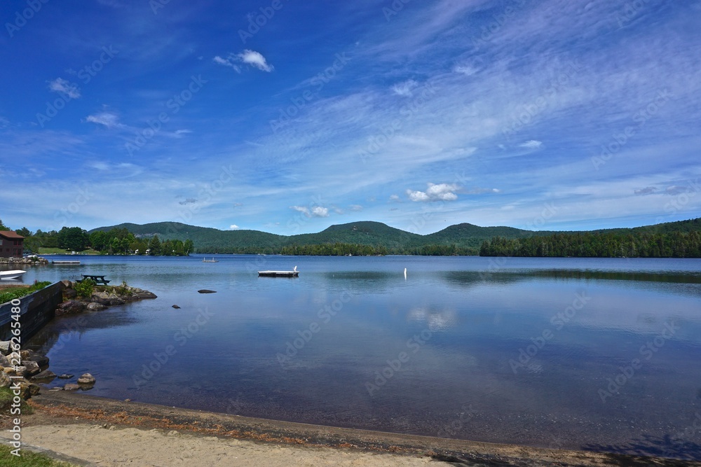 Adirondack Park, New York, USA: View of Blue Mountain in the distance from the shore of Blue Mountain Lake, with while clouds in a deep blue sky above.