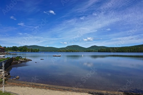 Fototapeta Naklejka Na Ścianę i Meble -  Adirondack Park, New York, USA: View of Blue Mountain in the distance from the shore of Blue Mountain Lake, with while clouds in a deep blue sky above.