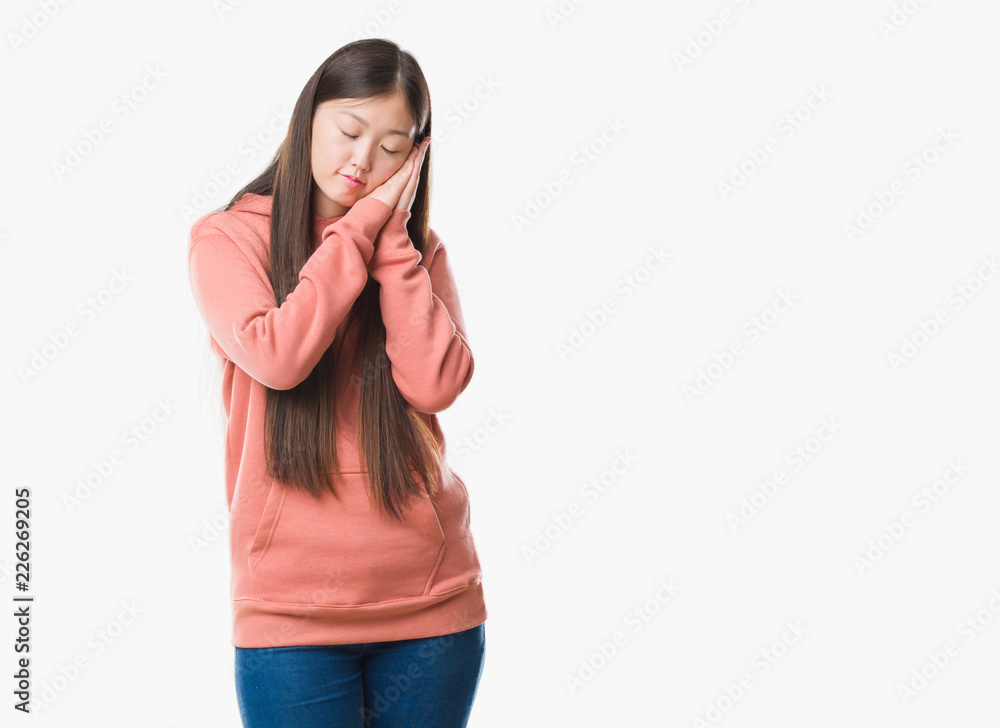Young Chinese woman over isolated background wearing sport sweathshirt sleeping tired dreaming and posing with hands together while smiling with closed eyes. Young Chinese woman over isolated background wearing sport sweathshirt sleeping tired dreaming and posing with hands together while smiling with closed eyes.