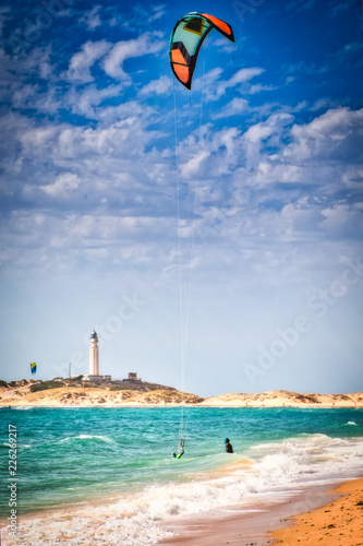 Surfers on the beach of Los Canos de Meca, with the Trafalgar lighthouse in the background, in southern Spain