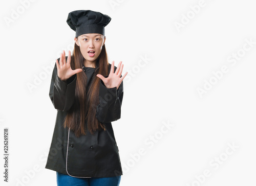 Young Chinese woman over isolated background wearing chef uniform afraid and terrified with fear expression stop gesture with hands, shouting in shock. Panic concept.