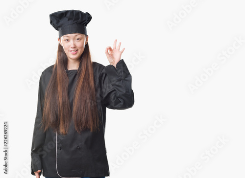 Young Chinese woman over isolated background wearing chef uniform smiling positive doing ok sign with hand and fingers. Successful expression.