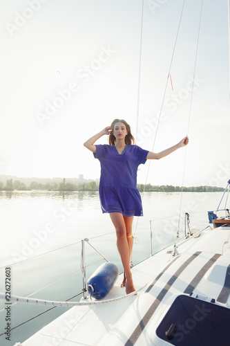 Attractive girl on a yacht at summer day. Close up of fashion portrait of stunning romantic woman posing yacht. Wearing an elegant dress, summer outfit. Blue sky. sunset
