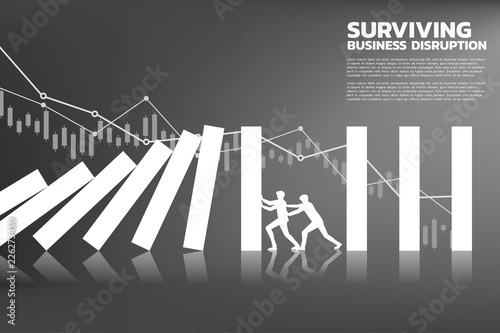 Silhouette of two businessman pushing for stop falling of domino with background graph. business concept of team try to stop the domino effect 