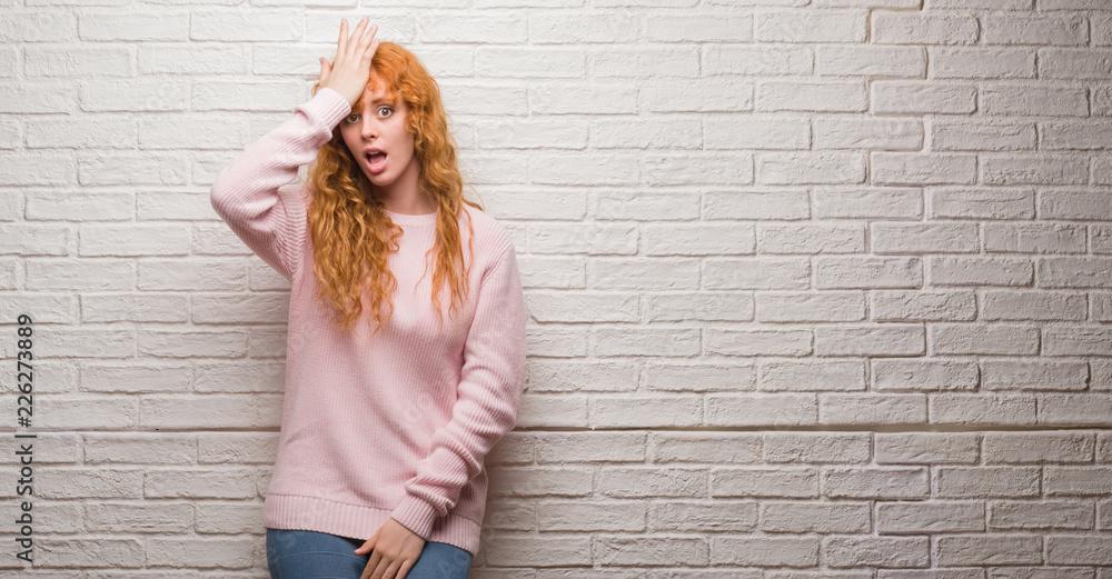 Young redhead woman standing over brick wall surprised with hand on head for mistake, remember error. Forgot, bad memory concept. Young redhead woman standing over brick wall surprised with hand on head for mistake, remember error. Forgot, bad memory concept.