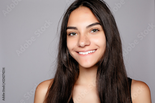 Portrait of a smiling attractive looking at the camera. Wearing black dress. Posing over grey background. Beautiful smiling woman with clean skin  natural make-up  and white teeth