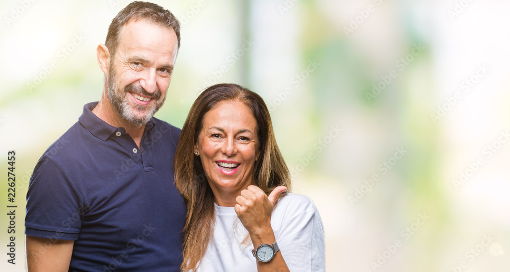 Middle age hispanic casual couple over isolated background smiling with happy face looking and pointing to the side with thumb up. Middle age hispanic casual couple over isolated background smiling with happy face looking and pointing to the side with thumb up.