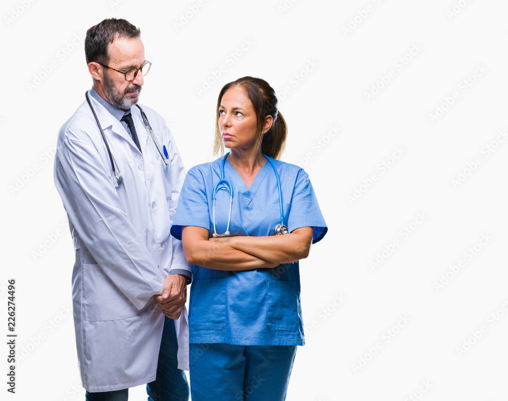 Middle age hispanic doctors partners couple wearing medical uniform over isolated background skeptic and nervous, disapproving expression on face with crossed arms. Negative person. Middle age hispanic doctors partners couple wearing medical uniform over isolated background skeptic and nervous, disapproving expression on face with crossed arms. Negative person.