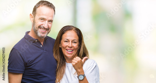 Middle age hispanic casual couple over isolated background smiling with happy face looking and pointing to the side with thumb up.