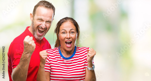 Middle age hispanic couple in love over isolated background celebrating surprised and amazed for success with arms raised and open eyes. Winner concept.