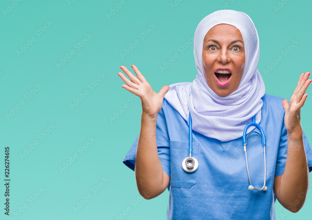 Middle age senior arab nurse woman wearing hijab over isolated background celebrating crazy and amazed for success with arms raised and open eyes screaming excited. Winner concept Middle age senior arab nurse woman wearing hijab over isolated background celebrating crazy and amazed for success with arms raised and open eyes screaming excited. Winner concept