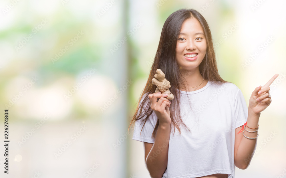 Young asian woman holding fresh organic over isolated background very happy pointing with hand and finger to the side Young asian woman holding fresh organic over isolated background very happy pointing with hand and finger to the side