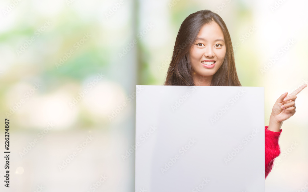 Young asian woman holding banner over isolated background very happy pointing with hand and finger to the side Young asian woman holding banner over isolated background very happy pointing with hand and finger to the side