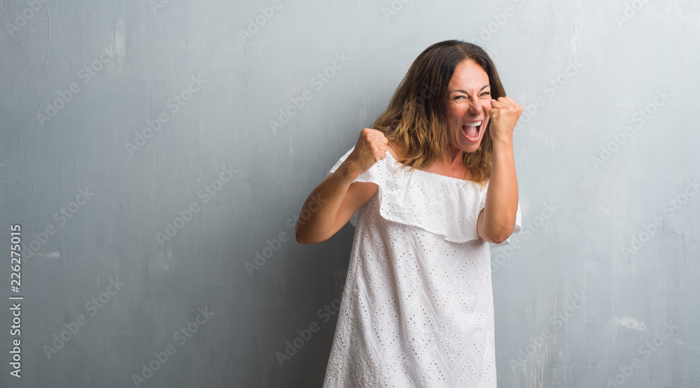 Middle age hispanic woman standing over grey grunge wall very happy and excited doing winner gesture with arms raised, smiling and screaming for success. Celebration concept. Middle age hispanic woman standing over grey grunge wall very happy and excited doing winner gesture with arms raised, smiling and screaming for success. Celebration concept.