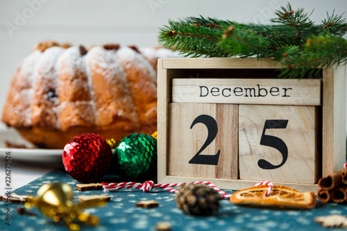 Traditional fruitcake for Christmas decorated with powdered sugar and nuts, raisins next to wooden calendar with date 25 december Delicioius Homemade Pastry. New year and Christmas celebration concept