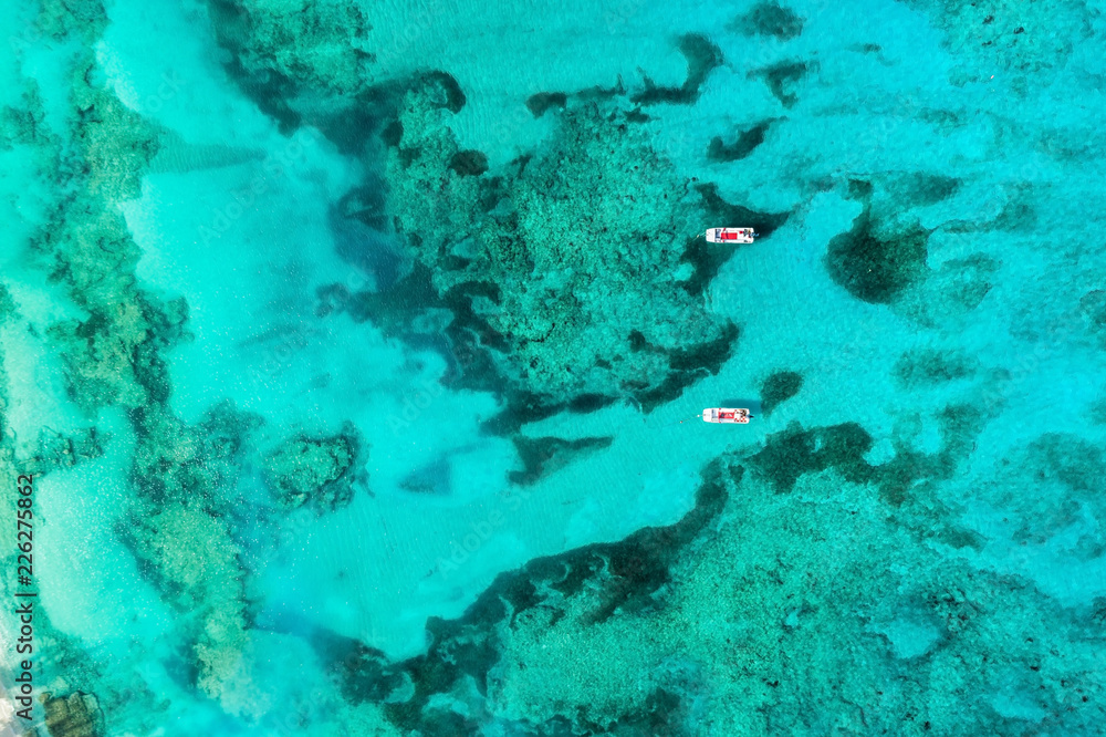Top view of amazing turquoise ocean water with colar reefs and two boats. Aerial view