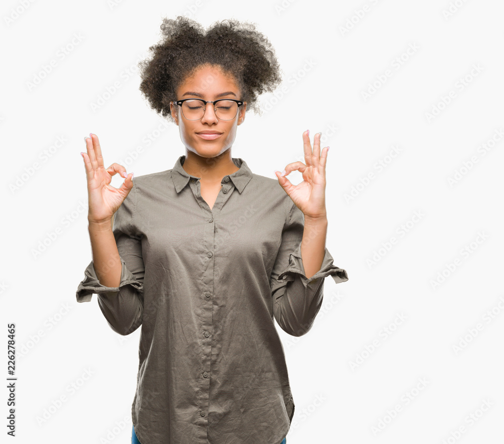 Young afro american woman wearing glasses over isolated background relax and smiling with eyes closed doing meditation gesture with fingers. Yoga concept. Young afro american woman wearing glasses over isolated background relax and smiling with eyes closed doing meditation gesture with fingers. Yoga concept.