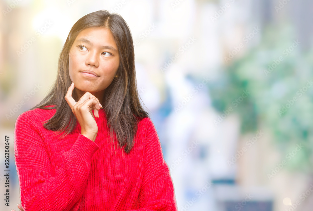 Young asian woman wearing winter sweater over isolated background with hand on chin thinking about question, pensive expression. Smiling with thoughtful face. Doubt concept. Young asian woman wearing winter sweater over isolated background with hand on chin thinking about question, pensive expression. Smiling with thoughtful face. Doubt concept.