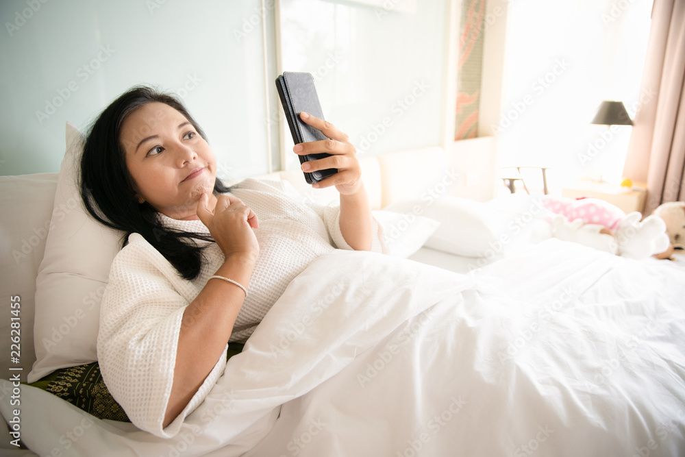 Woman sitting on white bed looking smartphone with frustration or angry Woman sitting on white bed looking smartphone with frustration or angry