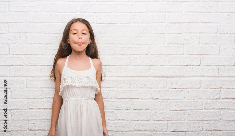 Young hispanic kid over white brick wall making fish face with lips, crazy and comical gesture. Funny expression.