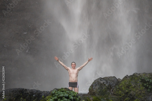 A happy man standing uder Sekumpul waterfall in Bali, Indonesia