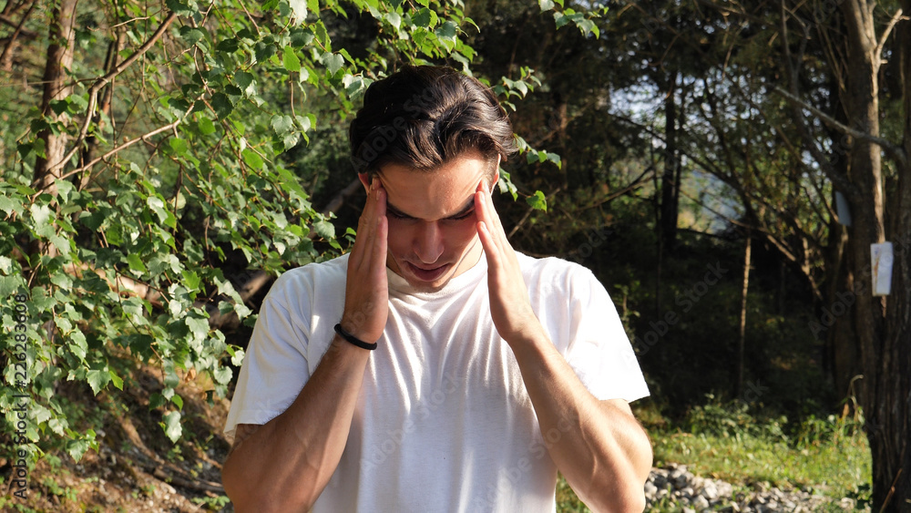 Young handsome man standing in nature, in pain, suffering from headache or migraine