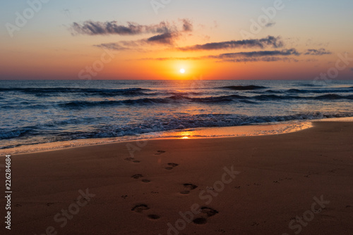 Amazing colorful sunrise at sea  footprints in the sand