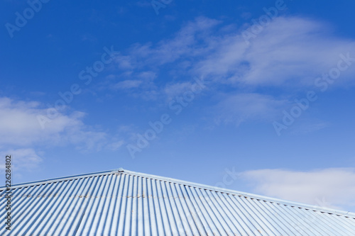 Blue tin corrugated tin roof with blue sky in the background. Sunny day.