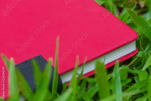 Red blank notebook or notepad on green grass.