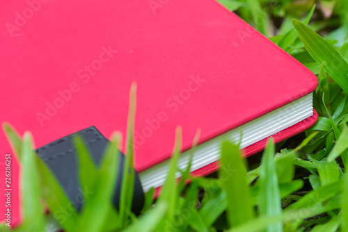 Red blank notebook or notepad on green grass.