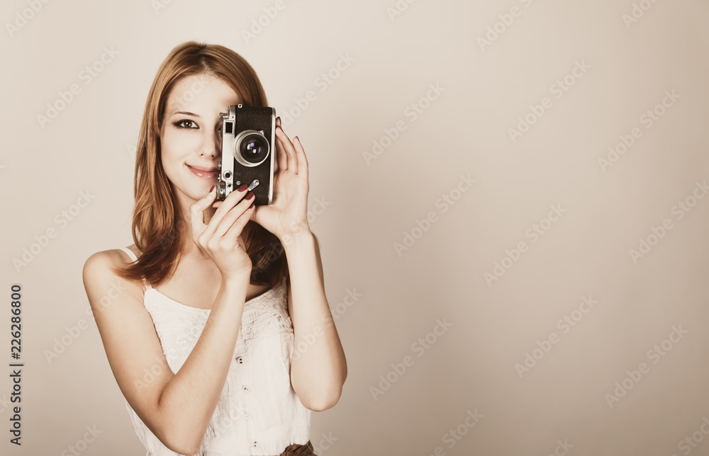 young redhead girl in a white dress holding a classic camera on a white background