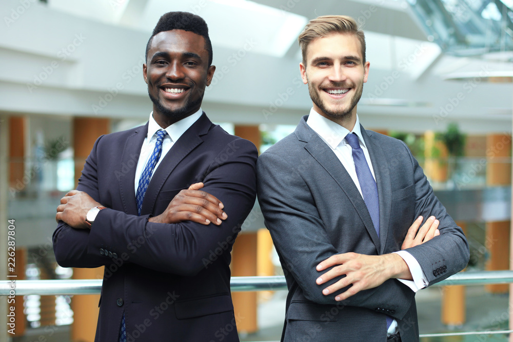 African american and caucasian business partners standing back to back together and looking in camera, in office. African american and caucasian business partners standing back to back together and looking in camera, in office.