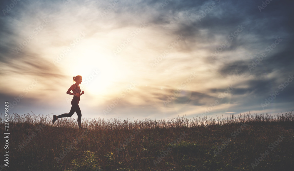 Young woman running on the field near seaside at sunset. Active person outdoors at the dusk in summer Young woman running on the field near seaside at sunset. Active person outdoors at the dusk in summer