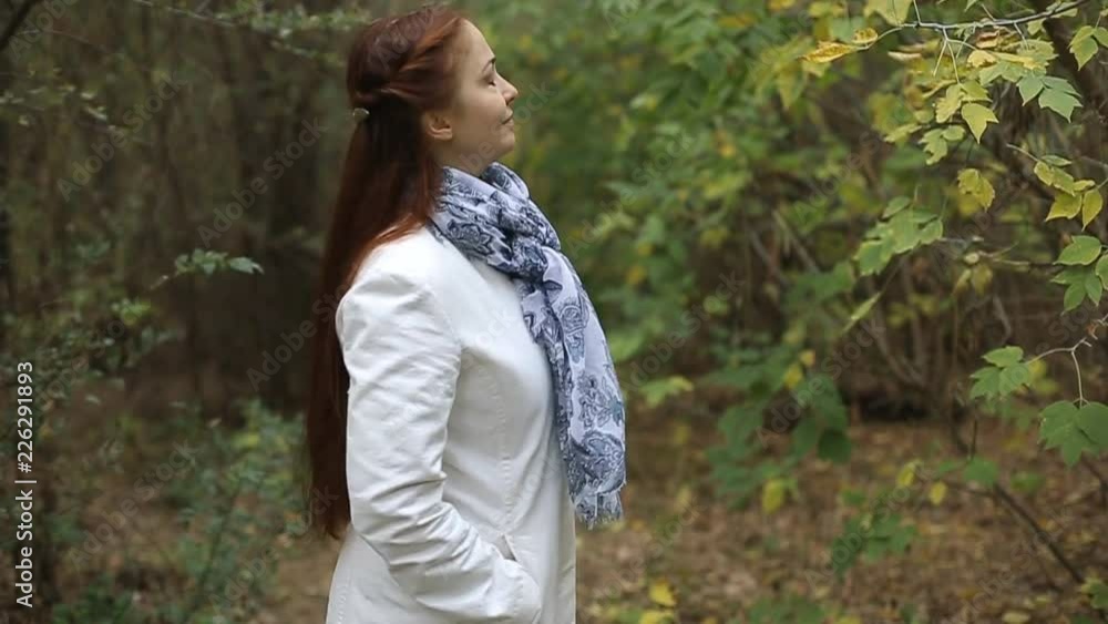 red-haired Caucasian middle-aged woman in a white coat walks on a cloudy day in the autumn park red-haired Caucasian middle-aged woman in a white coat walks on a cloudy day in the autumn park